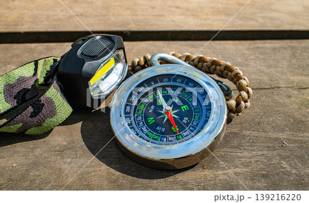 Magnetic compass with flashlight and paracord bracelet on wooden surface, outdoor survival hiking gear 139216220
