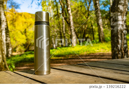 Thermos vacuum flask on wooden deck table with birch forest 139216222