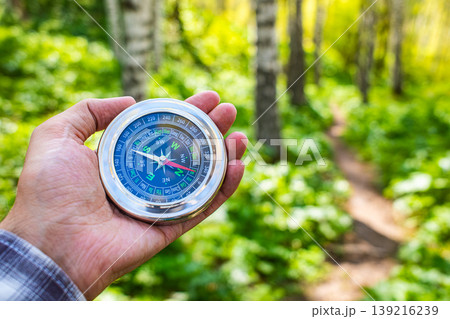 Hand holding round magnetic compass in green sunny forest, outdoor hiking navigation adventure travel 139216239