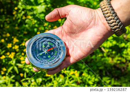 Hand holding magnetic compass in green mountain forest outdoor, hiking navigation adventure travel 139216287