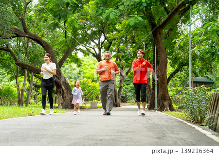Wide shot of Asian family with daughter, grandfather, mother and father are jogging together along the road in public park or garden with happiness. Wide shot of Asian family with daughter, grandfather, mother and father are jogging together along the road in public park or garden with happiness. 139216364
