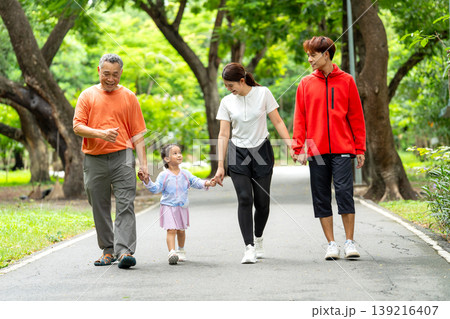 Close up Asian family with grandfather, grandchild, young mother and father hold hands and walk together along the road in public park or garden with happiness. Close up Asian family with grandfather, grandchild, young mother and father hold hands and walk together along the road in public park or garden with happiness. 139216407