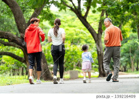 Back of Asian family with grandfather, grandchild, young mother and father are jogging together along the road in public park or garden with happiness. Back of Asian family with grandfather, grandchild, young mother and father are jogging together along the road in public park or garden with happiness. 139216409