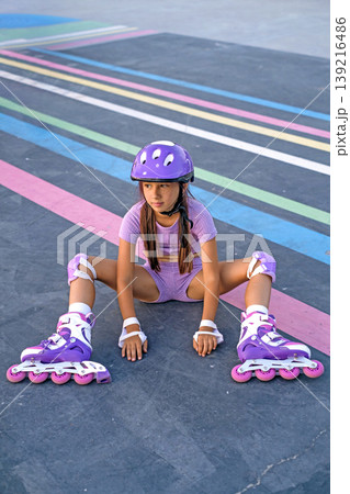 A girl with roller skates on sits on an asphalt path for skateboarding and roller skating. Sports hobbies 139216486
