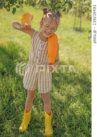 A laughing, cheerful child holds yellow squash. The child collected a fresh crop of vegetables in the garden A laughing, cheerful child holds yellow squash. The child collected a fresh crop of vegetables in the garden 139216491