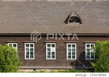 Rustic wooden house facade with a large thatched roof and white framed windows 139216688