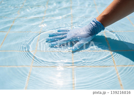 Hand wearing blue glove touching clear water surface in a tiled swimming pool Hand wearing blue glove touching clear water surface in a tiled swimming pool 139216816