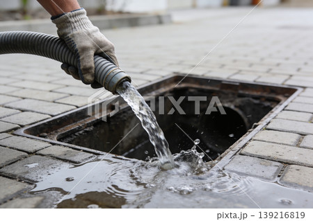 Worker's gloved hand directing water from a hose into a storm drain on a paved surface Worker's gloved hand directing water from a hose into a storm drain on a paved surface 139216819