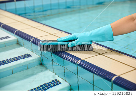 Hand in blue glove scrubbing pool edge tiles with a brush for cleaning and maintenance Hand in blue glove scrubbing pool edge tiles with a brush for cleaning and maintenance 139216825