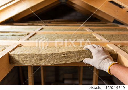 Attic insulation installation with mineral wool panels by a gloved hand Attic insulation installation with mineral wool panels by a gloved hand 139216840