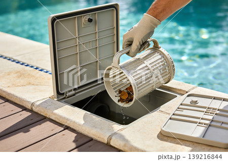 Pool maintenance worker emptying debris from a skimmer basket into the pool's filtration system 139216844