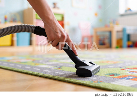 Close-up of a hand vacuuming a colorful children's rug in a bright playroom Close-up of a hand vacuuming a colorful children's rug in a bright playroom 139216869