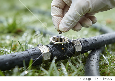 Gloved hand removing dirt from irrigation pipe fitting on wet grass 139216905