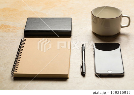 Desk essentials: notebook, pen, smartphone, and coffee mug arranged neatly on a textured surface Desk essentials: notebook, pen, smartphone, and coffee mug arranged neatly on a textured surface 139216913