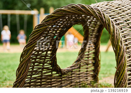 Woven willow tunnel structure in a playground with children playing in the background 139216919