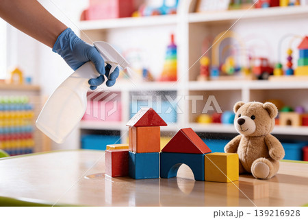 Gloved hand spraying disinfectant on children's toys and building blocks in a classroom 139216928