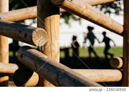 Close-up of wooden logs on a playground with blurred children playing in the background Close-up of wooden logs on a playground with blurred children playing in the background 139216930
