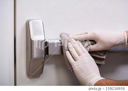 Person in white gloves cleaning a metal emergency exit bar with a cloth 139216938