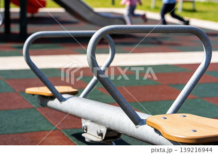 Close-up of a metal seesaw with wooden seats on a playground Close-up of a metal seesaw with wooden seats on a playground 139216944
