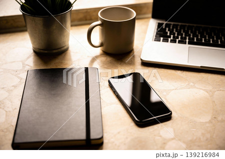 Modern desk setup with laptop, smartphone, notebook, and coffee mug on marble surface 139216984