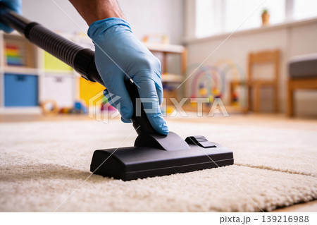 Close-up of gloved hands vacuuming a fluffy carpet in a child's playroom Close-up of gloved hands vacuuming a fluffy carpet in a child's playroom 139216988