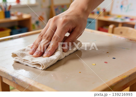 Hand wiping a messy art table with a damp cloth in a classroom setting Hand wiping a messy art table with a damp cloth in a classroom setting 139216993