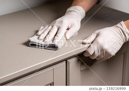 Hands wearing white gloves wiping down a beige countertop with a microfiber cloth Hands wearing white gloves wiping down a beige countertop with a microfiber cloth 139216999