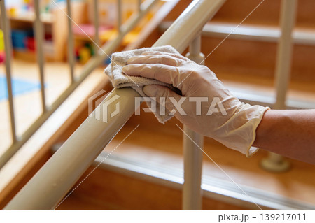 Hand in glove wipes down a stair railing with a cloth, emphasizing hygiene and safety 139217011