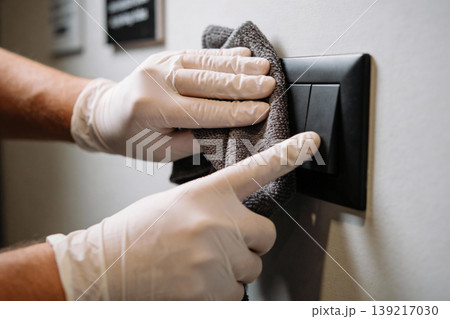 Hands wearing white gloves cleaning a black light switch with a dark gray cloth Hands wearing white gloves cleaning a black light switch with a dark gray cloth 139217030