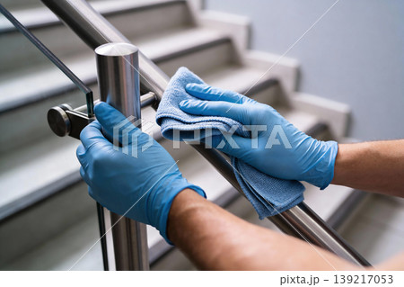 Person wearing blue gloves cleaning a metal handrail with a microfiber cloth on stairs Person wearing blue gloves cleaning a metal handrail with a microfiber cloth on stairs 139217053