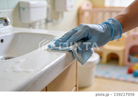 Hand wearing blue glove wiping down a bathroom sink counter with a blue cloth 139217056