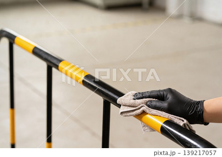Hand wearing black glove wipes down a yellow and black striped safety railing with a cloth 139217057