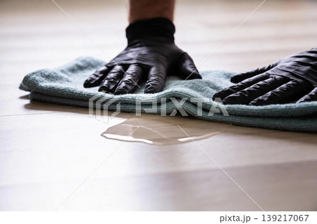 Hands in black gloves wiping up spilled liquid from a light-colored floor with a cloth Hands in black gloves wiping up spilled liquid from a light-colored floor with a cloth 139217067