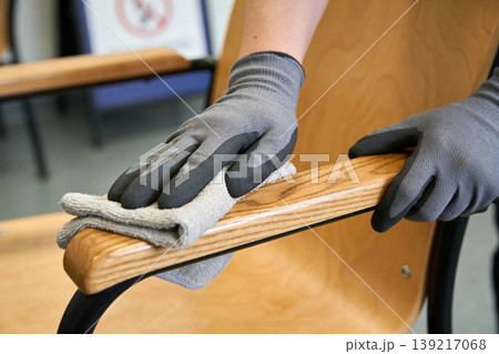 Person wearing gloves wipes down a wooden chair armrest with a microfiber cloth Person wearing gloves wipes down a wooden chair armrest with a microfiber cloth 139217068
