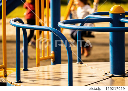 Close-up of a blue and yellow playground merry-go-round with children playing in the background 139217069