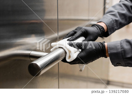 Person in black gloves cleaning a stainless steel handrail with a white cloth Person in black gloves cleaning a stainless steel handrail with a white cloth 139217080