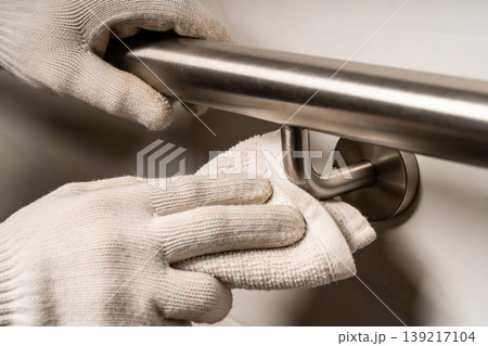Hands wearing white gloves cleaning a brushed metal grab bar with a white cloth Hands wearing white gloves cleaning a brushed metal grab bar with a white cloth 139217104