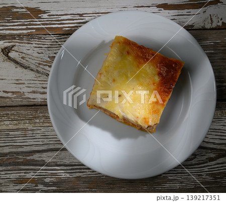 Savory slice of baked lasagna served on a white plate with rustic wooden background Savory slice of baked lasagna served on a white plate with rustic wooden background 139217351