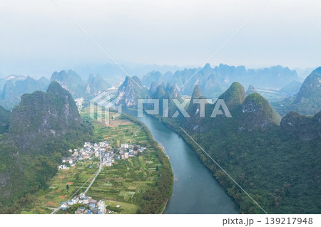 Lush karst peaks rise steeply from the calm river waters. China Lush karst peaks rise steeply from the calm river waters. China 139217948