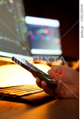 Trader using mobile app with financial charts at desk Trader using mobile app with financial charts at desk 139219345