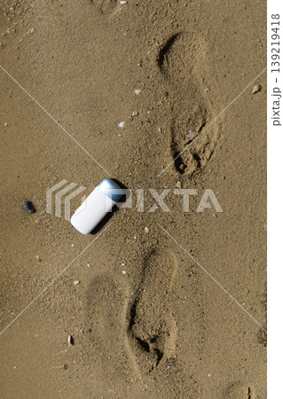 Essential sunscreen bottle lying on golden wet beach sand with footprints Essential sunscreen bottle lying on golden wet beach sand with footprints 139219418
