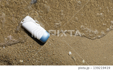 White and blue product container in shallow ocean water on sunlit sandy beach. White and blue product container in shallow ocean water on sunlit sandy beach. 139219419