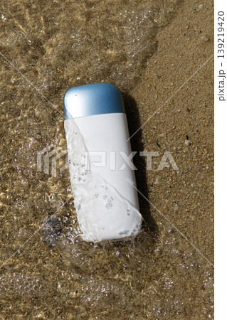White cosmetic bottle with blue cap in clear ocean water on textured sand beach White cosmetic bottle with blue cap in clear ocean water on textured sand beach 139219420