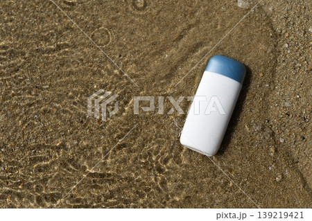 White skincare product bottle with blue cap on wet beach sand and clear water White skincare product bottle with blue cap on wet beach sand and clear water 139219421