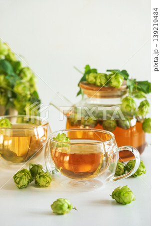 Hop Tea in Glass Teapot and Glass Cups on White Wooden Table Hop Tea in Glass Teapot and Glass Cups on White Wooden Table 139219484