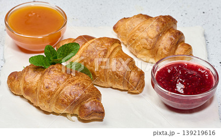 Three fresh golden croissants on a white board with fruit jam and mint Three fresh golden croissants on a white board with fruit jam and mint 139219616