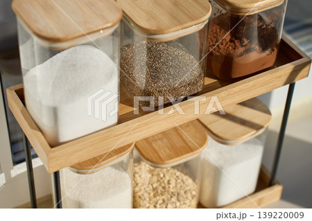Glass jars with wooden lids stand on bamboo shelf with dry ingredients 139220009