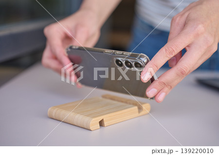Hands place smartphone on wooden stand on kitchen counter 139220010
