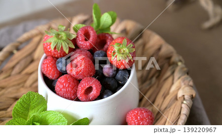Fresh Summer Berries with Mint in a Ceramic Bowl on a Woven Tray 139220967