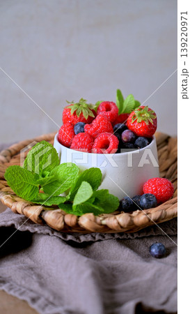 Fresh Assorted Berries and Mint in a White Ceramic Bowl on a Woven Tray 139220971